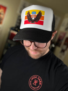 A man with glasses and his head tilted down showing the black and white foam trucker hat on his head that has a swooping bald eagle on it.