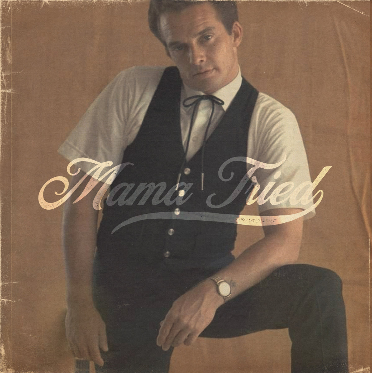 Seated man holding a guitar with cream Mama Tried lettering
