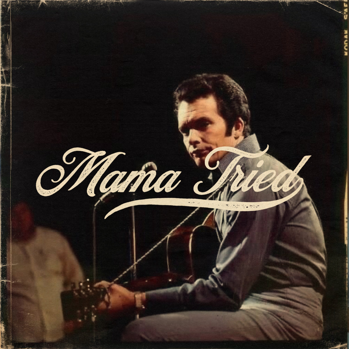 Man performing with a guitar and white Mama Tried lettering